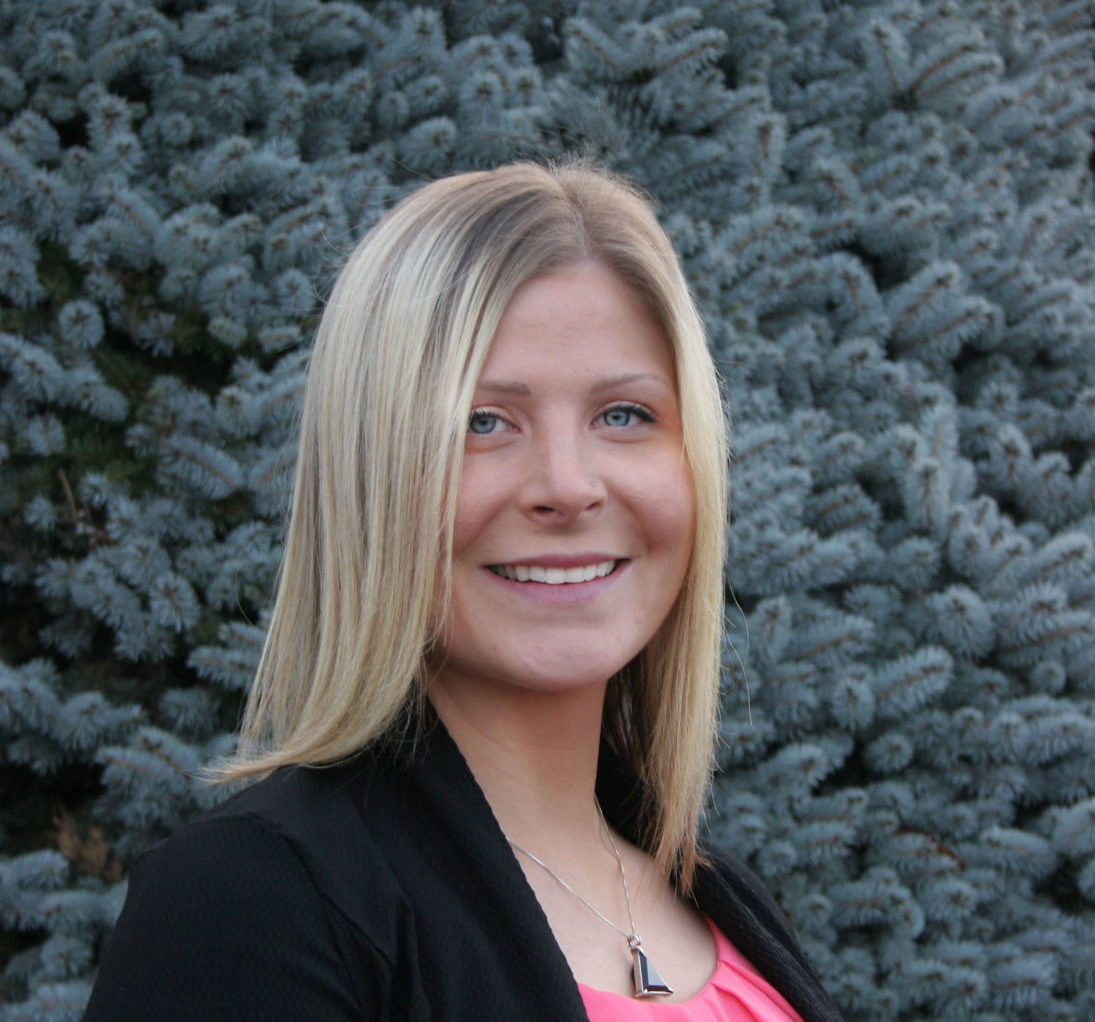 a smiling woman standing in front of a pine tree
