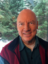 a man standing in front of pine trees while smiling at the camera