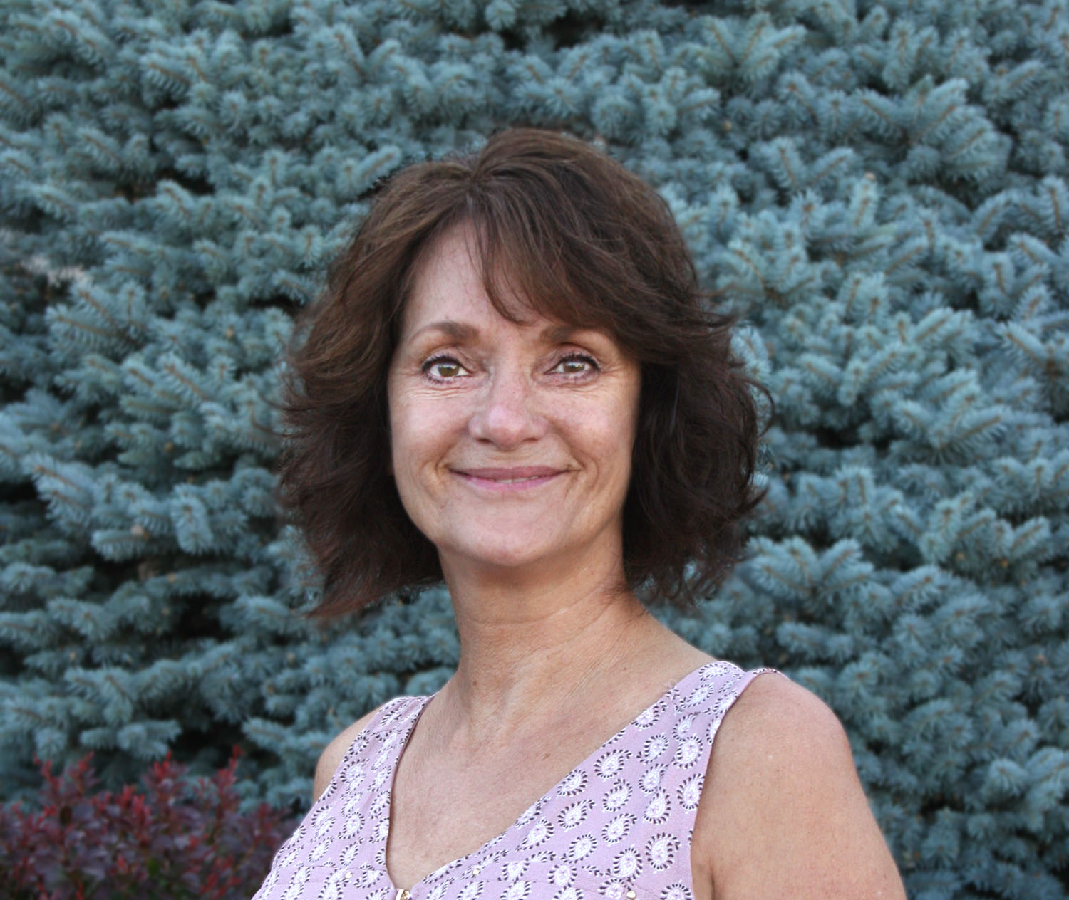 a smiling woman standing in front of a pine tree