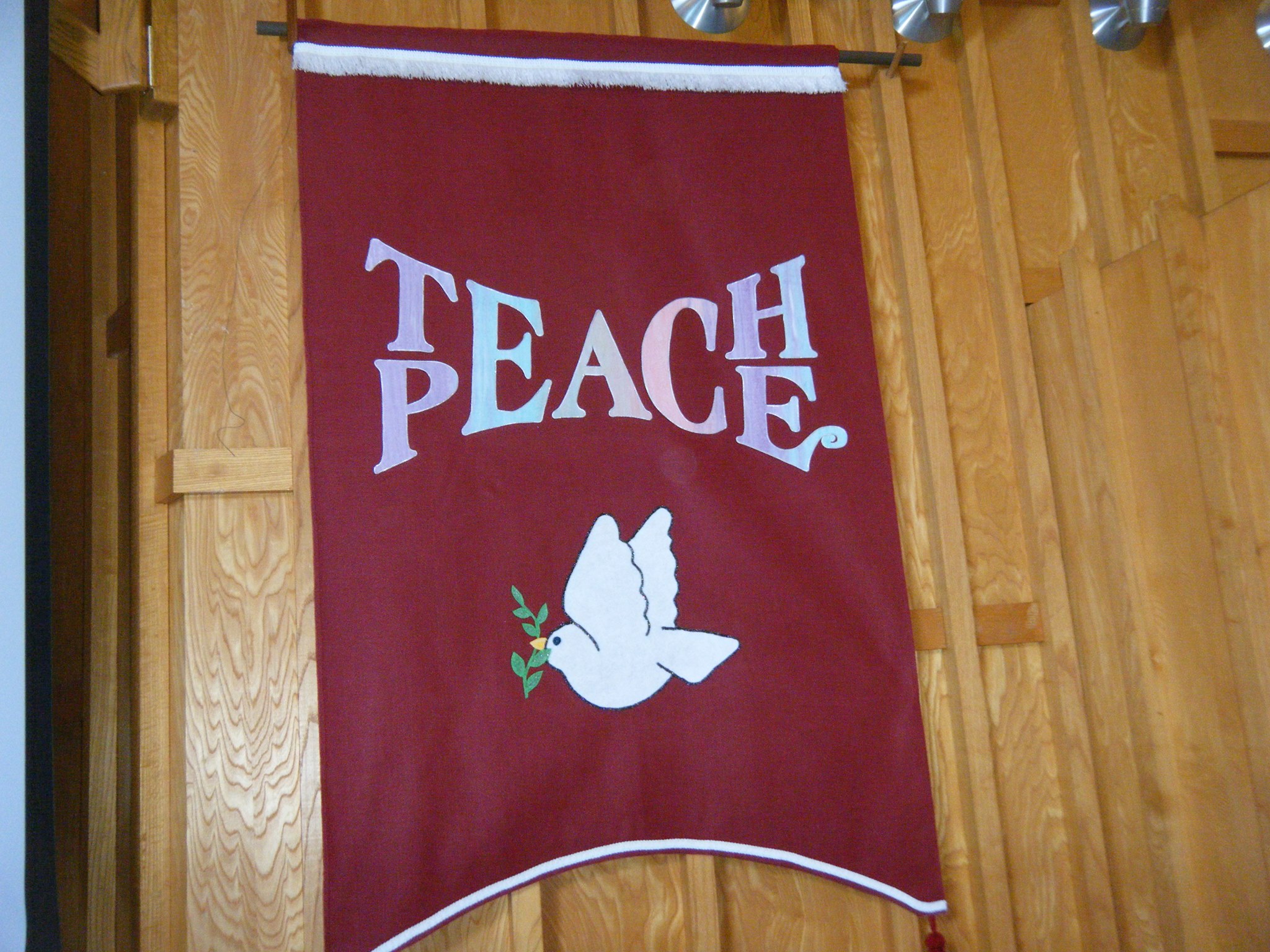 a red banner with a dove hung on a wood wall that reads, "teach peace"