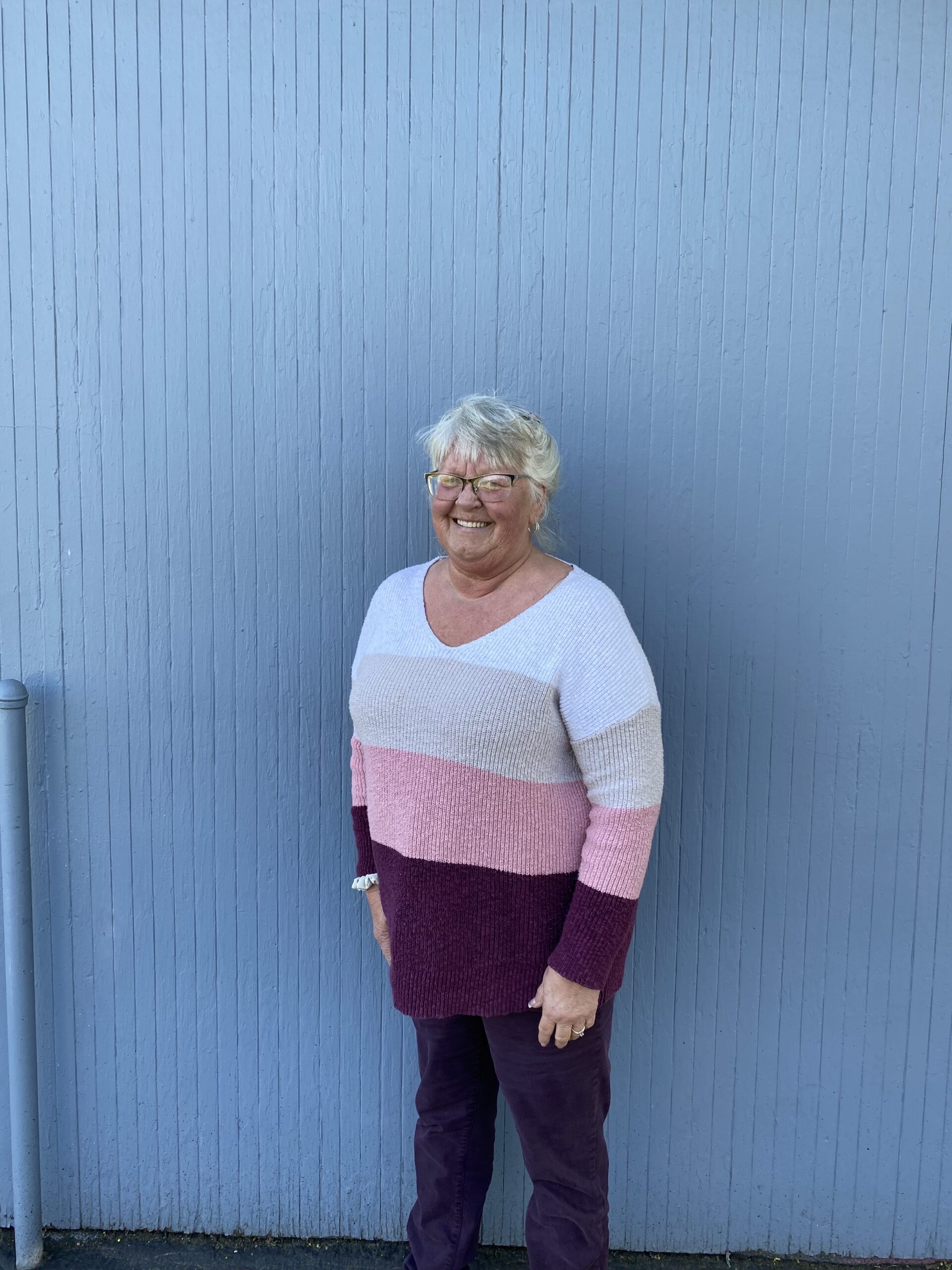 a smiling woman wearing a color-blocked sweater with her back against a periwinkle blue wall