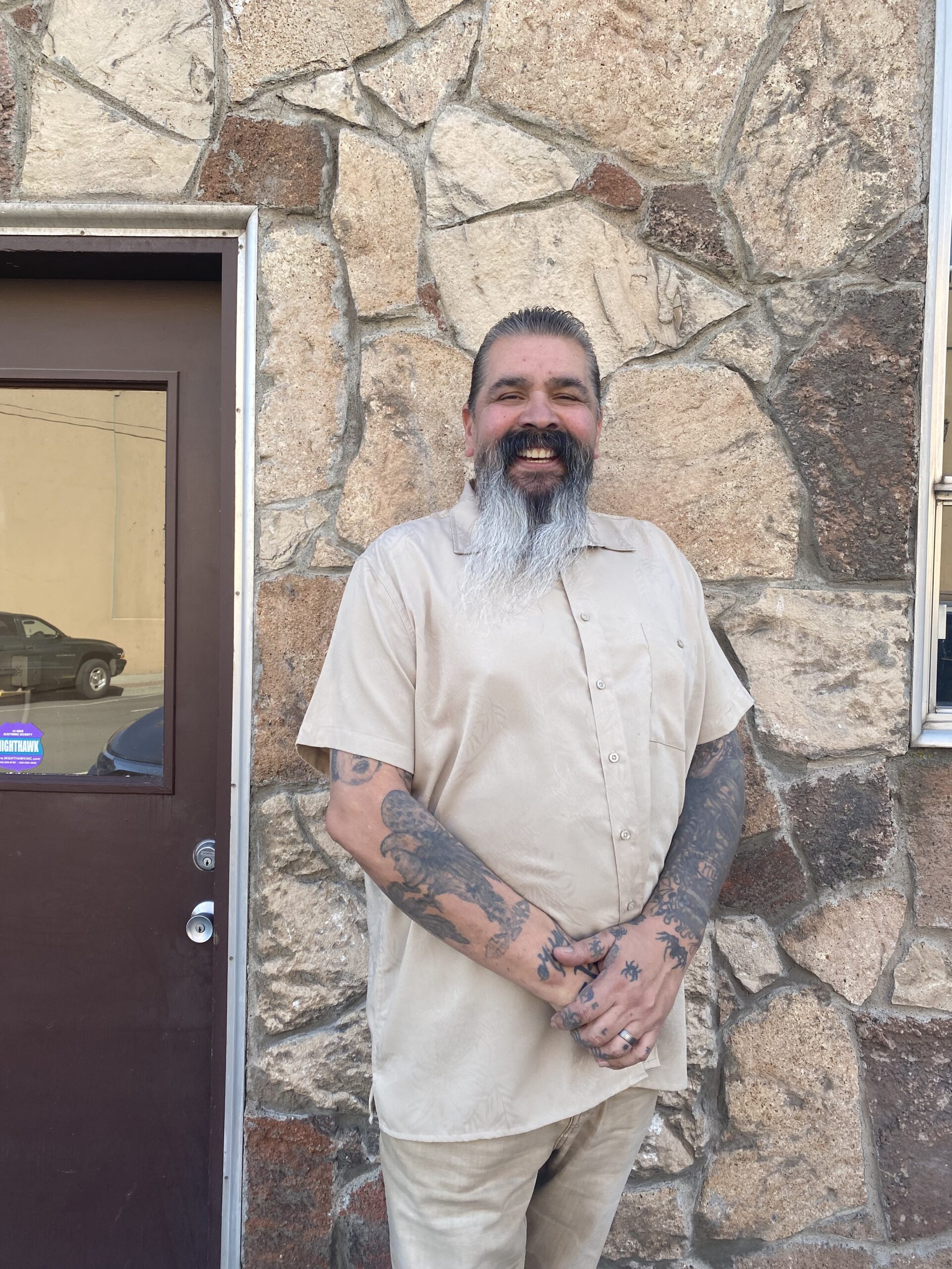 a smiling adult man standing in front of a flagstone wall