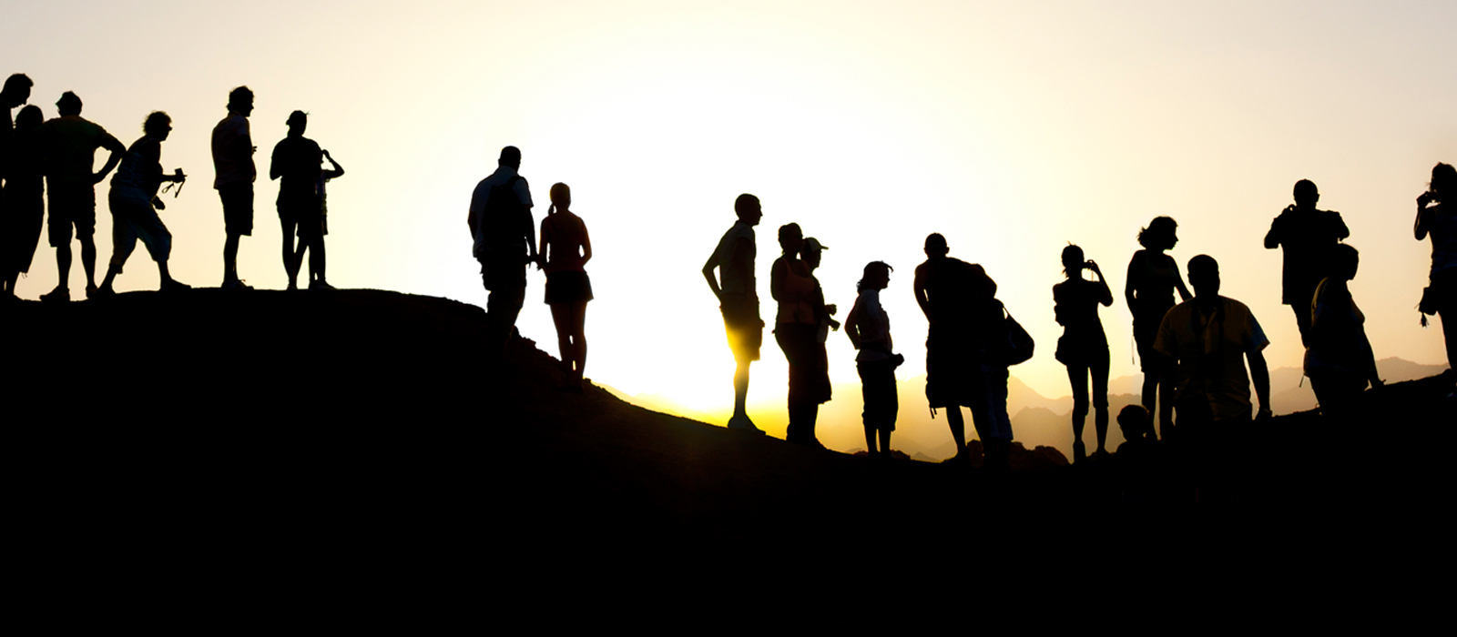 a group of people standing on a hill, silhouetted by the bright, warm, yellow sun in the background