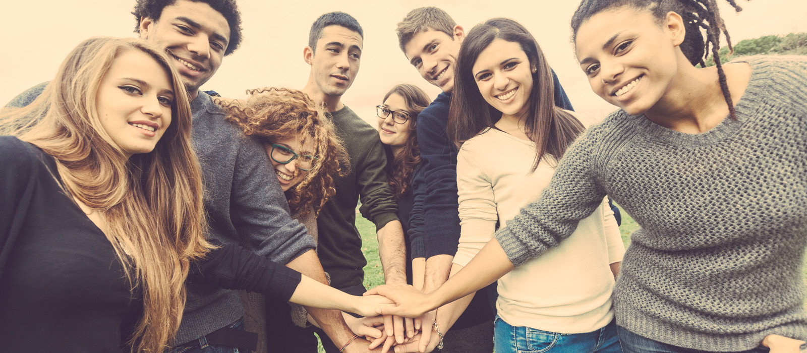 a smiling group of diverse young adults all putting their hands on top of eachother