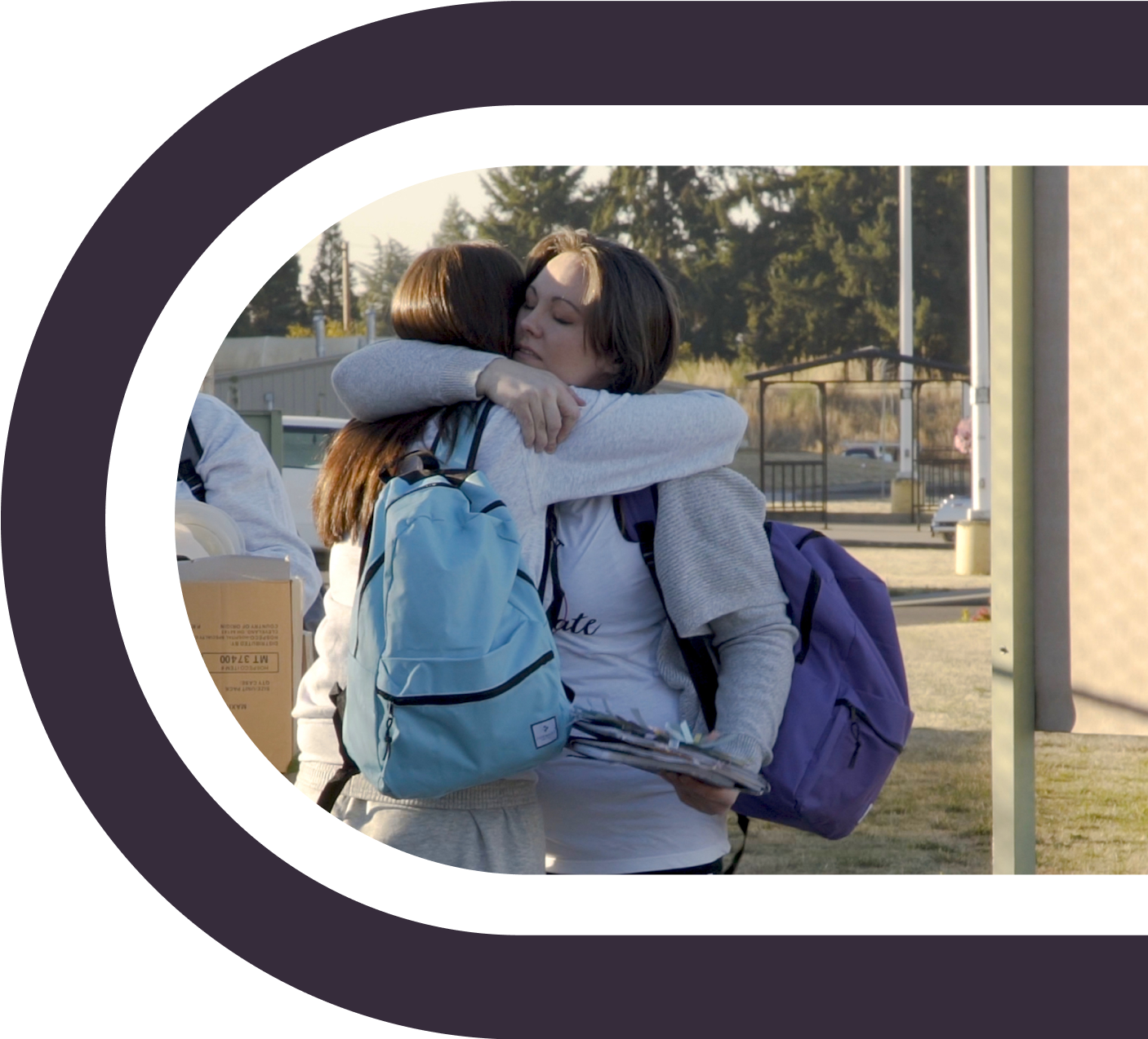 a woman wearing sweats and a backpack lovingly hugging a girl wearing sweats and a backpack