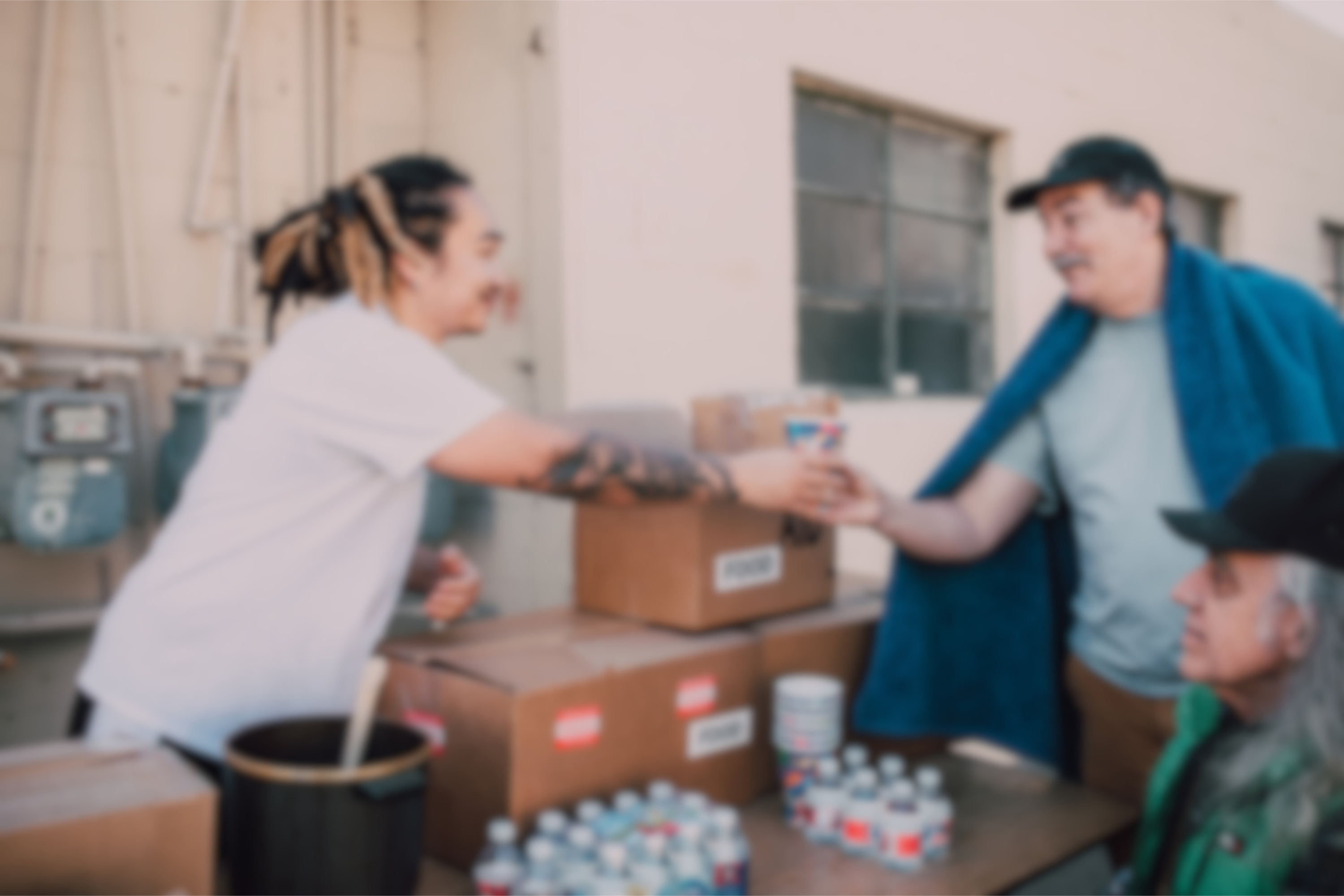 a person with long hair hands a cup to two people in need of help